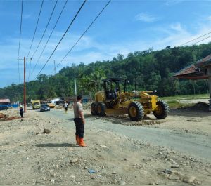 Personel Brimob melakukan pengawasan perbaikan jalan raya Desa Garoga menggunakan dua unit alat berat jenis motor grader.